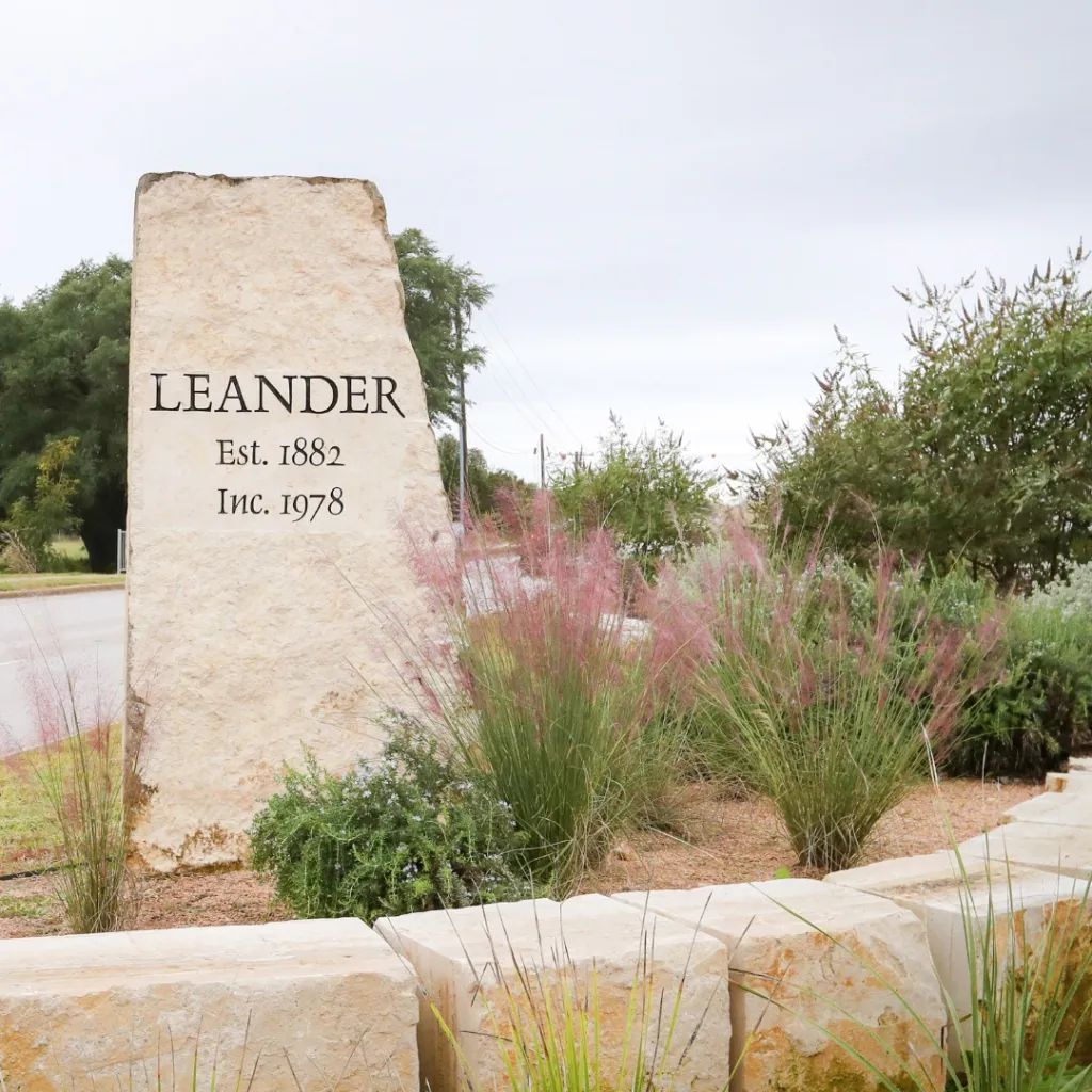 The Leander, Texas limestone welcome monument — engraved "Leander, Est. 1882, Inc. 1978" — framed by native pink muhly grass