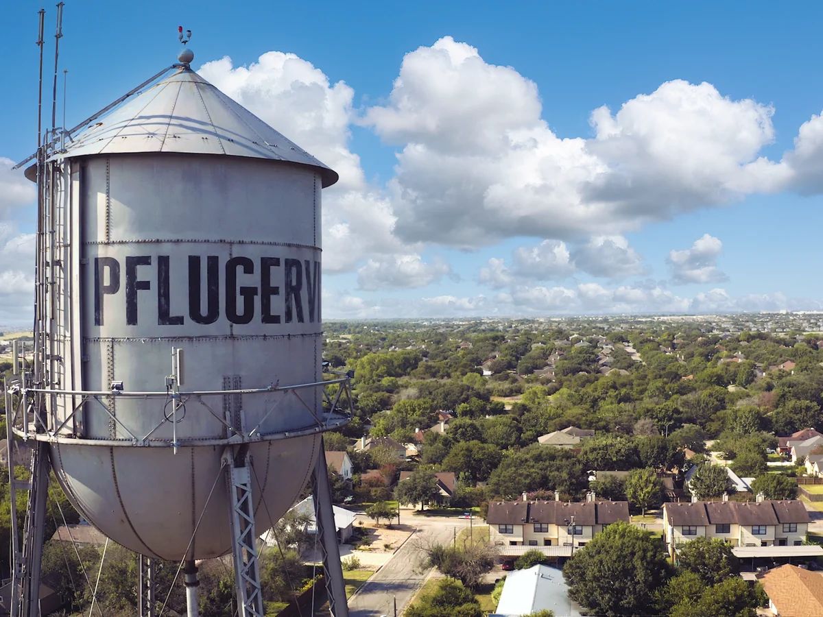 The iconic silver Pflugerville water tower rising above the city's tree-lined neighborhoods under a bright blue Texas sky